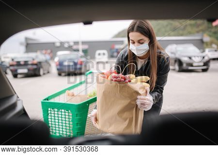 Over Trunk View Of Young Woman In Medical Mask In Masks Loading Bags In Trunk After Supermarket Shop