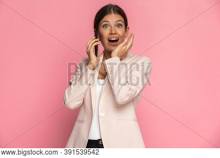 cute businesswoman being happily surprised by some news on the phone against pink background
