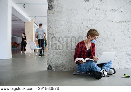 Young Student With Laptop Sitting On Floor Back At College Or University, Coronavirus Concept.