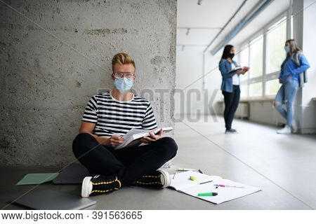 Young Student With Face Mask Sitting On Floor Back At College Or University, Coronavirus Concept.