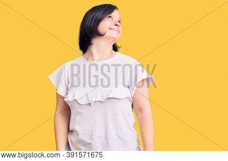 Brunette woman with down syndrome wearing casual white tshirt looking away to side with smile on face, natural expression. laughing confident. 