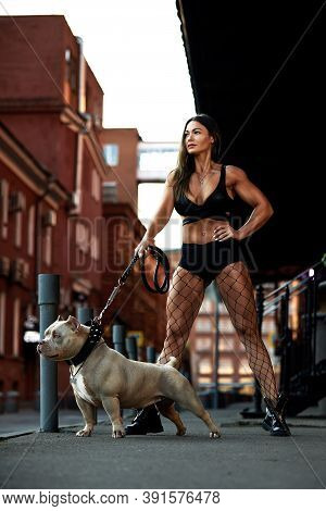 Sexy And Srong Brunette Woman Posing With Bully Dog On City Street, Looking At Camera.