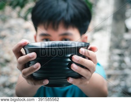 Hungry Boy Holding Empty Black Bowl Waiting For Food For Sustenance With Unhappy. Asking Help Food D