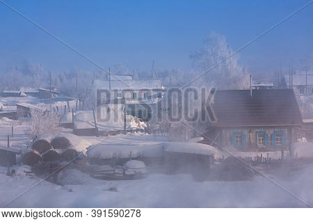 Winter Landscape In The Fog With A Small Village In Russia. Small Snow-covered Houses, Smoke From Ch