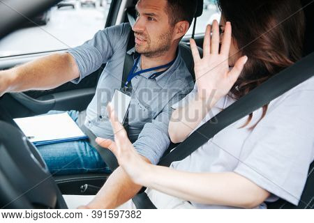 Male Driving Instructor Holds Steering Wheel And Try To Avoid A Car Accident. Young Woman Raised Her