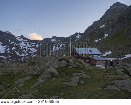 Evening Sunset Summer View Of Bremer Hutte, An Alpine Mountian Wooden Hut With Snow-capped Moutain P