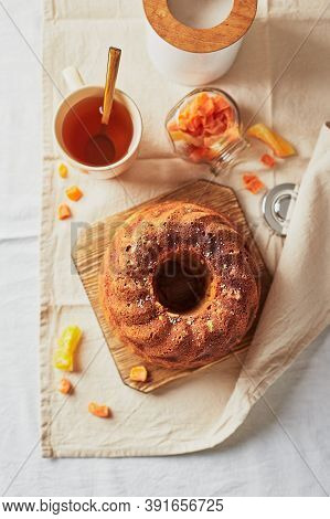 Homemade Autumn Carrot Cake With Candied Fruits On Wooden Cutting Board And Cup Of Tea On Light Back