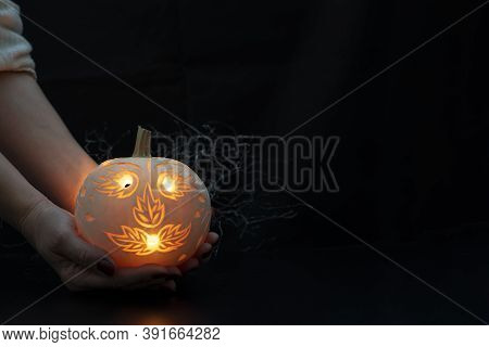 Hands Holding A Carved Pumpkin With Candle Inside On Black Background