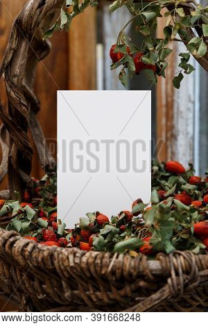 Blank White Greeting Card And Old Graceful Basket. Mockup With Vintage Basket Of Vines And Rose Hips