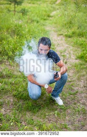 Bearded Vape Man Is Resting On The Grass And Vaping And Letting Off Steam From An E-cigarette. Moder