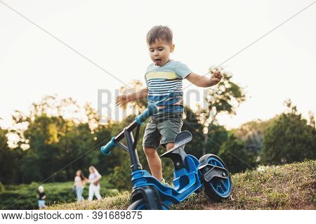 Cute Caucasian Boy Is Playing With A Bike Outside In A Park On A Green Field Celebrating Children Da