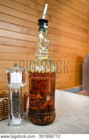 On The Table Are A Glass Bottle Filled With Spicy Olive Oil With Chili And Rosemary And A Salt And P