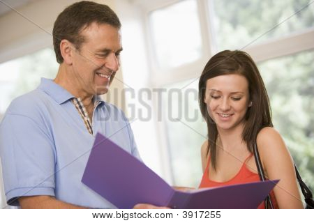 Teacher In Corridor Talking To Student With Notebooks