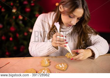 Traditionalist Concept. Cute Brunette Young Woman Icing Christmas Gingerbread With Christmas Tree An