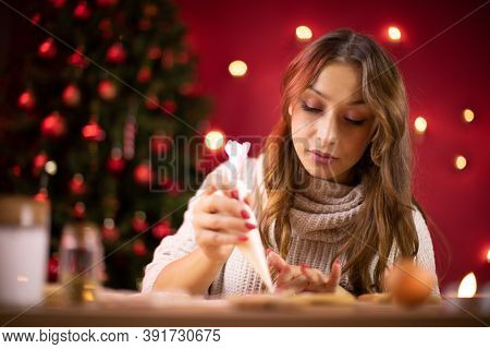 Christmas Bakery. Pretty Brunette Girl Decorating Christmas Gingerbread Cookies On Blurred Backgroun