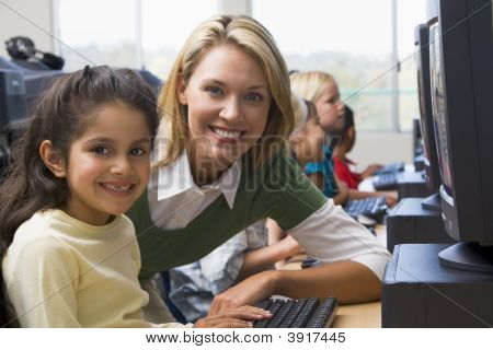 Insegnante aiutare studenti al Computer Terminal con gli studenti In Background (profondità di campo/High Key)
