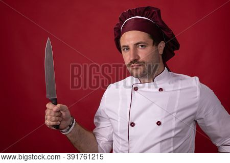 Unshaven Handsome Male Chef Cook Holding Chefs Knife Looking At Camera Isolated On Red Background. P