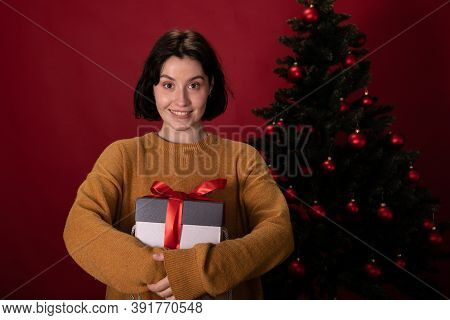 Smiling Dressed Casually Brunette Girl Embraced Gift Box With Christmas Present Looking At Camera On