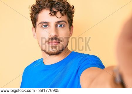 Young caucasian man with curly hair wearing casual clothes taking a selfie thinking attitude and sober expression looking self confident 