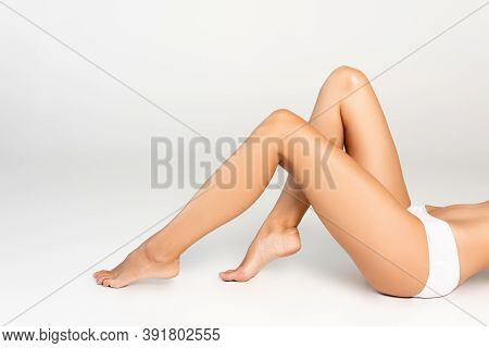 Cropped Of Woman Lying In White Underpants With Smooth Legs On Grey