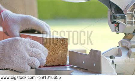 Carpenter In Protective Gloves Precisely Sets Wooden Workpiece Into Mitre Saw And Mitres Bar. Circul