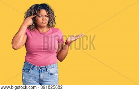 Young african american plus size woman wearing casual clothes confused and annoyed with open palm showing copy space and pointing finger to forehead. think about it. 