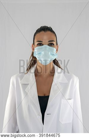 Attractive Female Doctor With Virus Protection Mask Looking Straight Ahead And White Background.