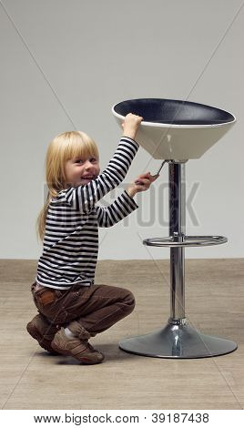 สาวบลอนด์ 3 ปีในกางเกงยีนส์อยู่บนเก้าอี้สูง