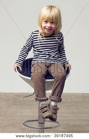 สาวบลอนด์ 3 ปีในกางเกงยีนส์อยู่บนเก้าอี้สูง
