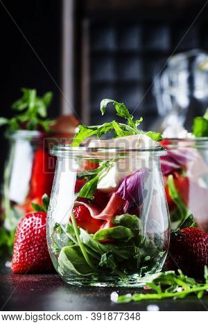 Summer Salad With Arugula, Soft Cheese, Red Strawberry And Prosciutto In Glass Jars On Black Table, 