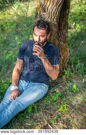 Stylish Bearded Vaper Enjoying An Electronic Cigarette In The Calm Outdoors. Electronic Cigarette As
