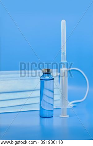 Transparent Medical Ampoules, Syringe And Protective Mask On A Light Blue Background. Concept: Medic