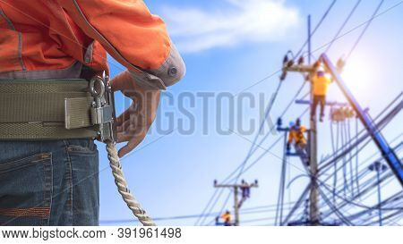 Midsection Of Electrician Lineman Wearing Safety Belt With Blurred Background Of Electrical Workers 