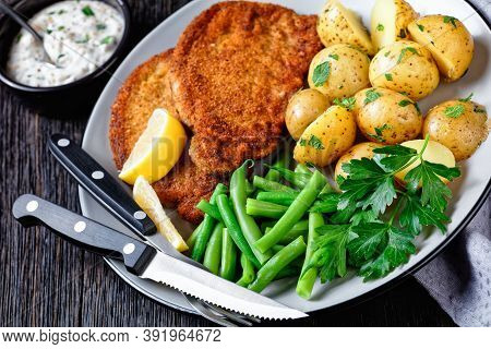German Pork Schnitzel With Young Potatoes, Green Beans With Cutlery Served On A Plate With Lemon Wed