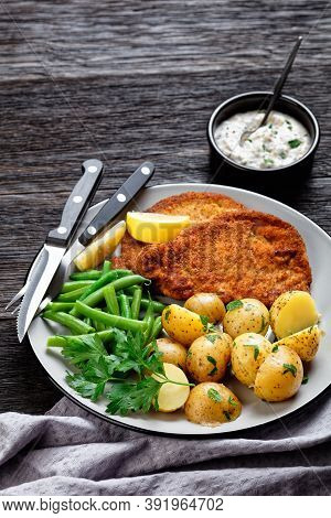 German Pork Schnitzel With Young Potatoes, Green Beans With Cutlery Served On A Plate With Lemon Wed