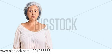 Senior woman with gray hair wearing bohemian style puffing cheeks with funny face. mouth inflated with air, crazy expression. 