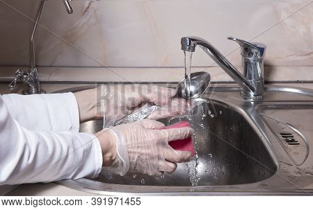 Woman's Hands With Gloves Washing Dish With Fresh Water At Kitchen Faucet Over The Metal Sink. Human
