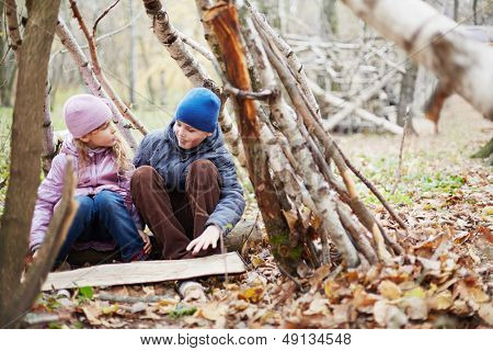 Piccolo ragazzo e ragazza sedersi nella capanna costruita tra betulle in autunno parco e parlare