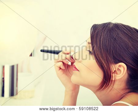 Portrait of attractive young adult woman applying blusher in her bathroom