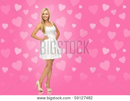beauty, fashion and valentines day concept - smiling woman in white dress and high heels over pink background with hearts