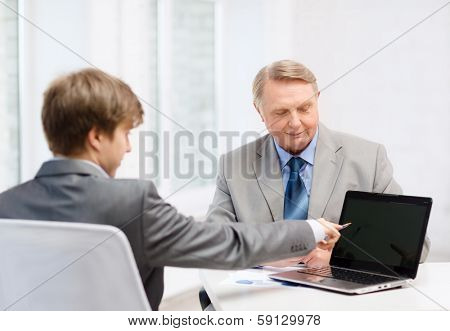 business, advertisement, technology and office concept - older man and young man with laptop computer in office