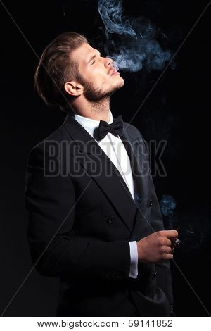 side of an elegant man enjoying his cigar on dark studio background