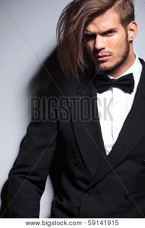 cutout picture of an elegant young fashion man with long hair in tuxedo  looking at the camera.on gray background 