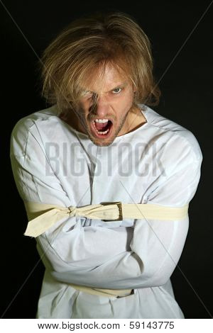 Mentally ill man in strait-jacket on black background