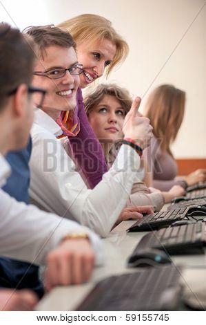 Happy students with professor in schoolroom by computers