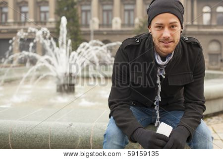 Young Smiling Man With Mobile Phone In Front of Fountan, Urban Space