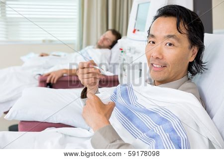 Portrait of male cancer patient eating crushed ice during dialysis at hospital room