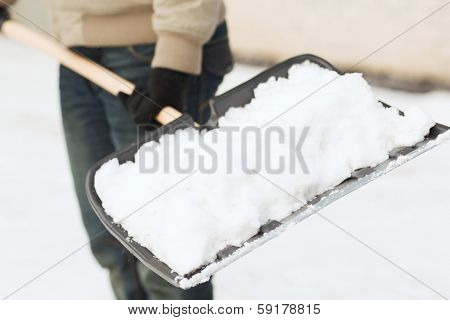 winter and cleaning concept - closeup of man shoveling snow from driveway