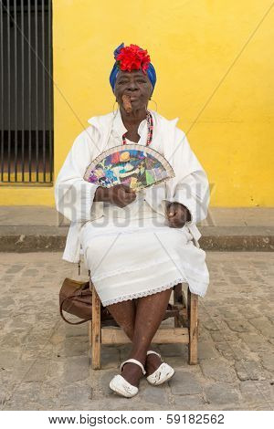 HAVANA,CUBA - JANUARY 20, 2014:Old black lady smoking a huge cuban cigar and wearing a typical dress with afrocuban religious necklaces
