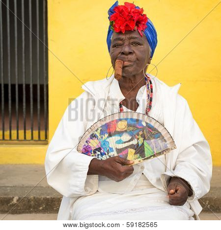 HAVANA,CUBA - JANUARY 20, 2014:Old black lady smoking a huge cuban cigar and wearing a typical dress with afrocuban religious necklaces